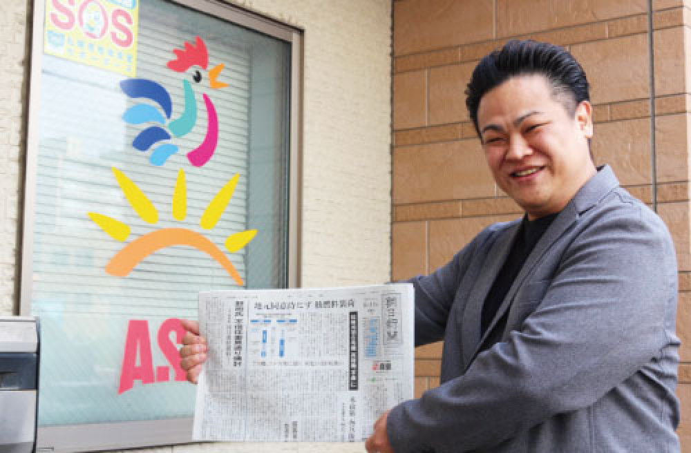 新聞を手に笑顔の佐藤さん