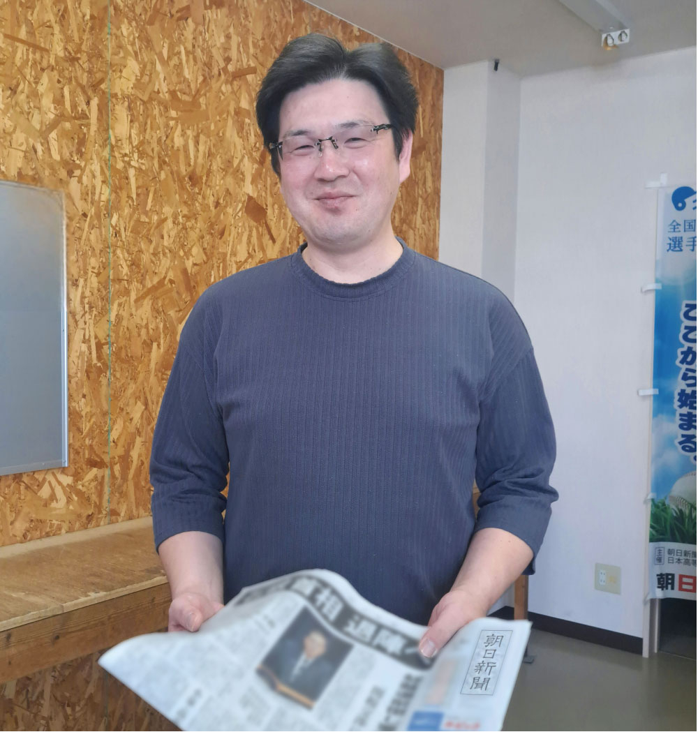 新聞を手に微笑む廣田輝政所長