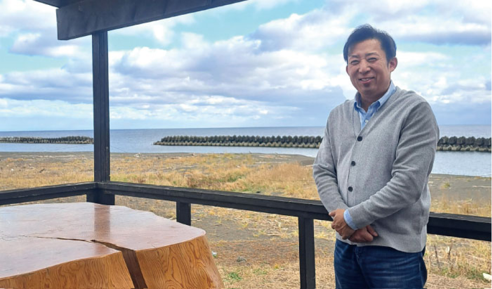 虎杖浜を背に少し寒そうな佐々木所長