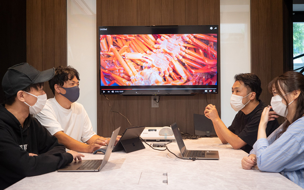 撮影してきたカニの映像を見ながらネットショップの戦略を立てる、ネットワンの水野治人社長(左端)と田中さん(隣)。ここのスタッフはみんな若い。