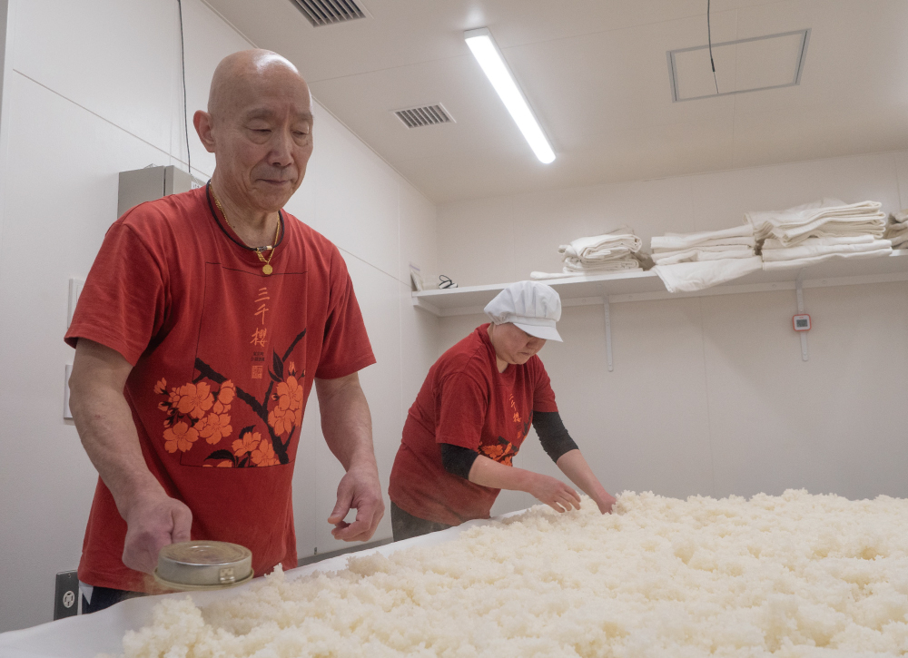 麹室で蒸し米を広げる山田耕司さん(左)と浦里美智子さん。